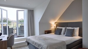 Quarto de hotel moderno com uma cama grande, uma escrivaninha e vista para o exterior.