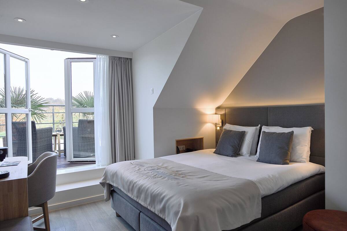 A modern hotel room with a large bed, a desk, and a view of the outdoors.