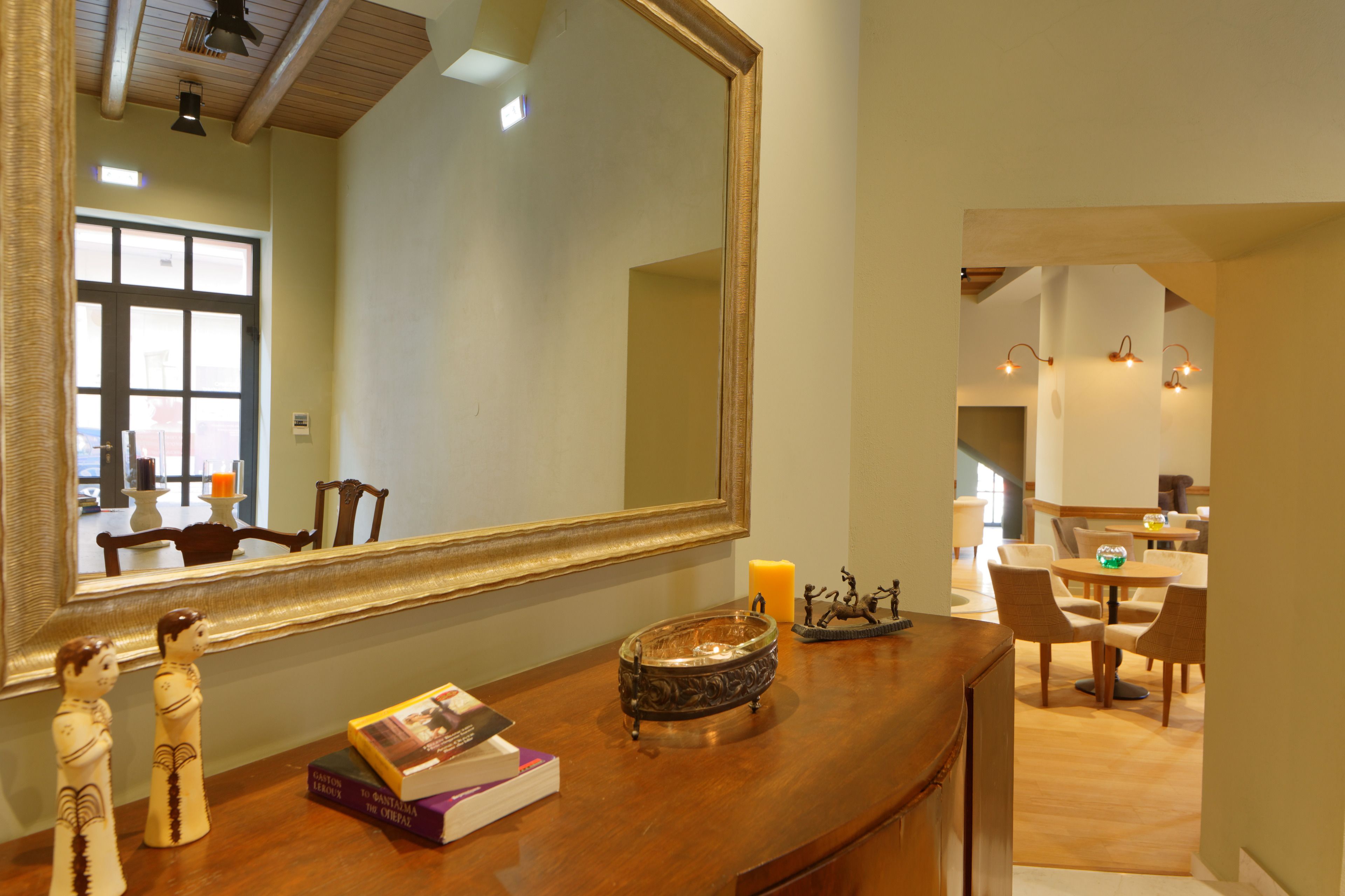Una habitación bien iluminada con un espejo grande, muebles de madera y un comedor visible a través de un vano abierto.