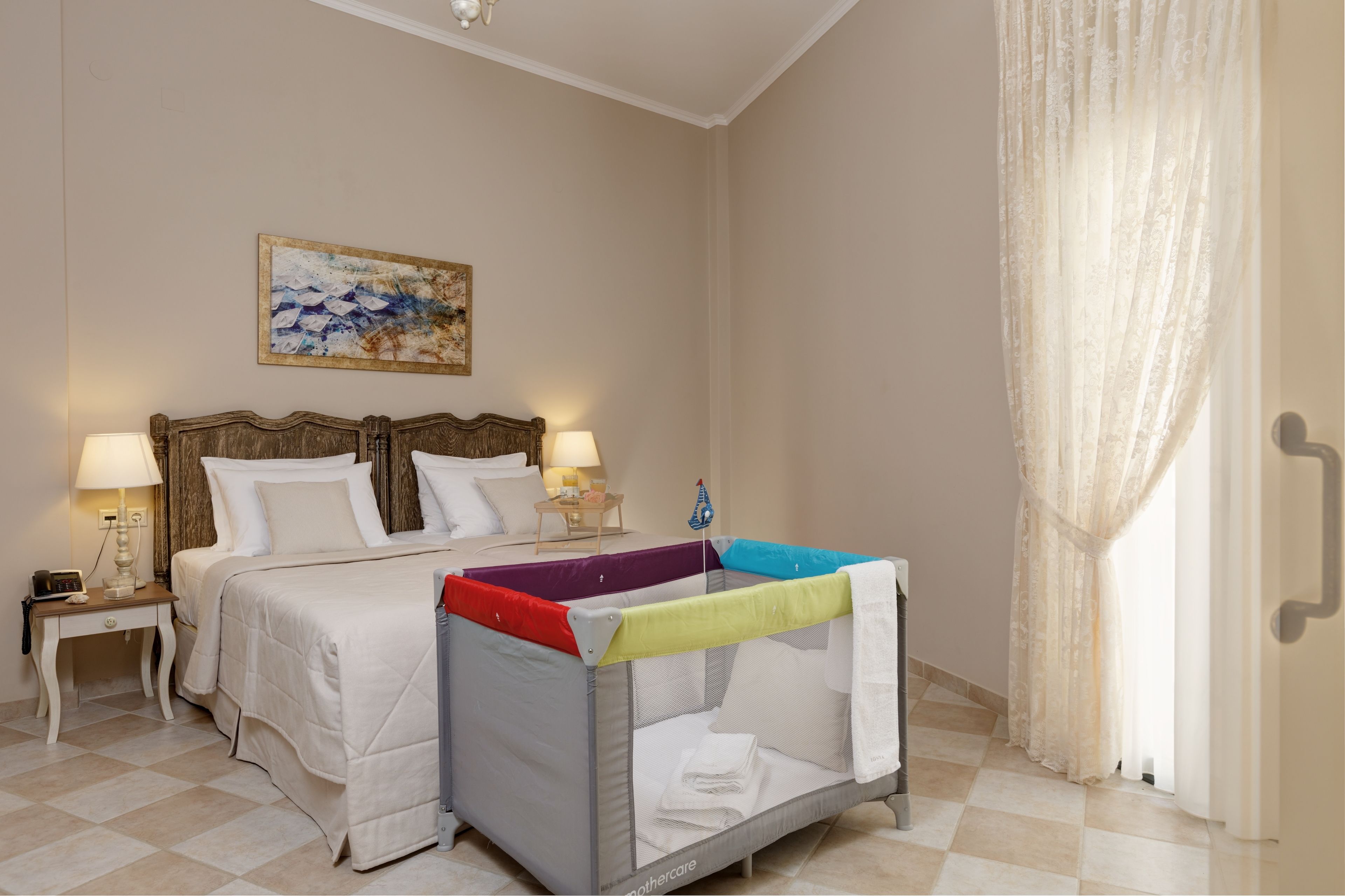 Quarto de hotel com cama, berço, mesa de cabeceira com abajur e um quadro na parede.