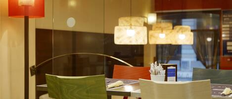 A modern dining area with glass partitions, red and green chairs, and a table with a menu.