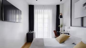 Een moderne hotelkamer met een bed, een bureau, een stoel, een televisie en een raam met dunne gordijnen.