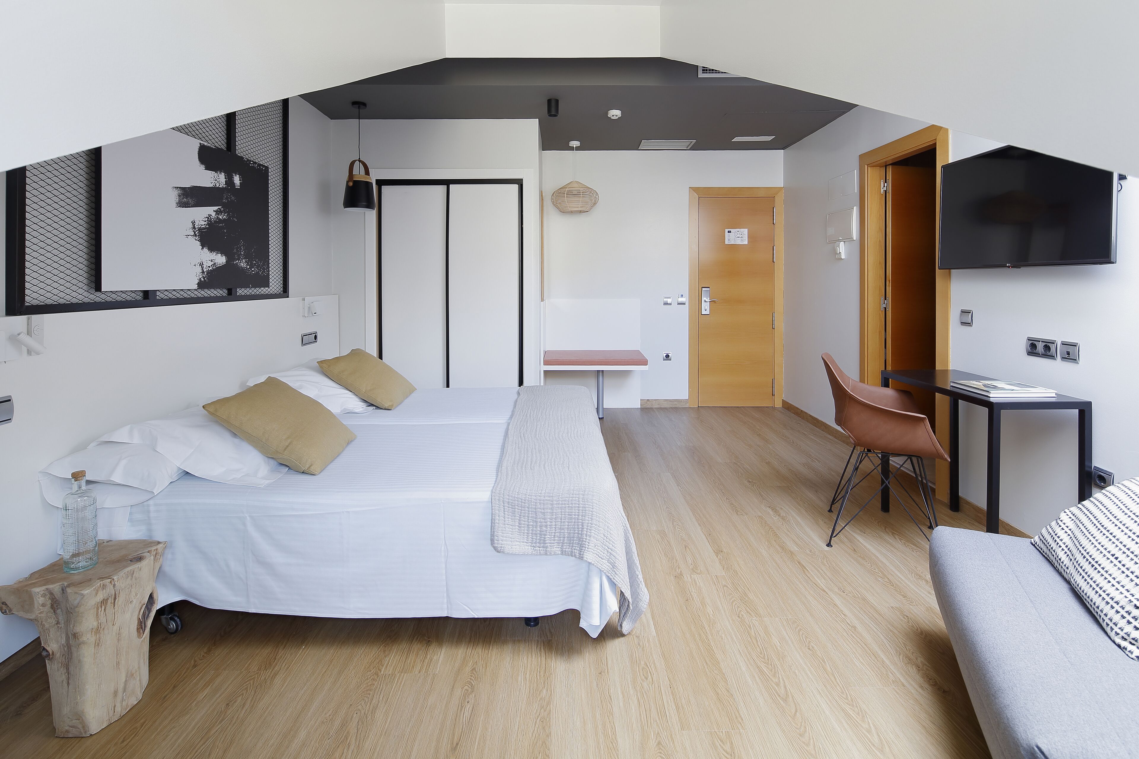 Un dormitorio moderno con dos camas, un escritorio, una silla, un televisor y suelo de madera.