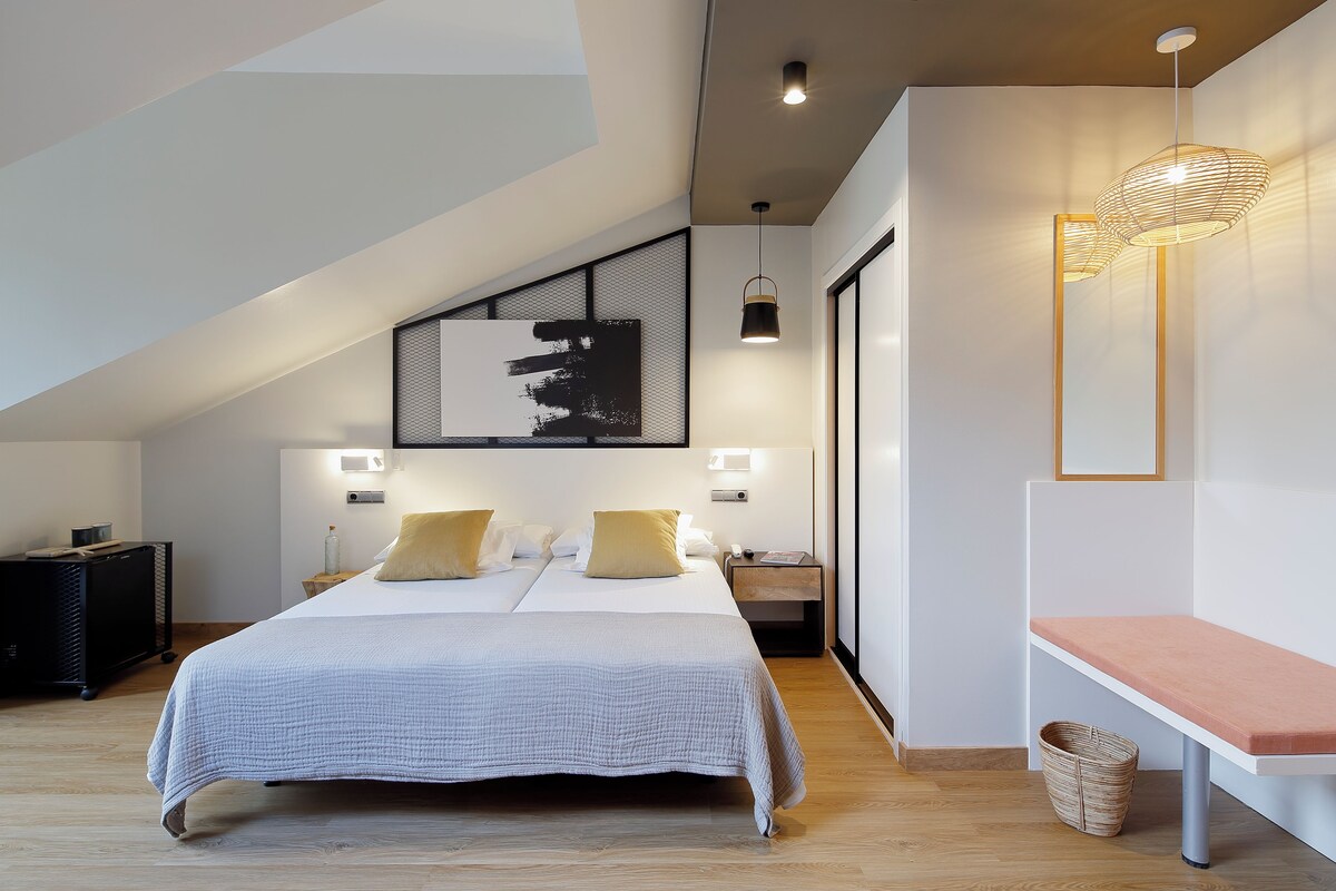 Un dormitorio moderno con una cama grande, un banco y una lámpara fijada a la pared.