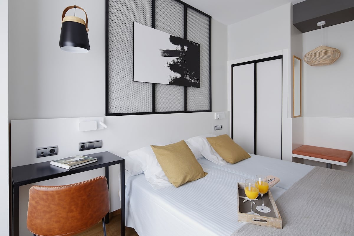 A modern hotel room with a bed, bedside table, chair, and a tray with glasses of orange juice.