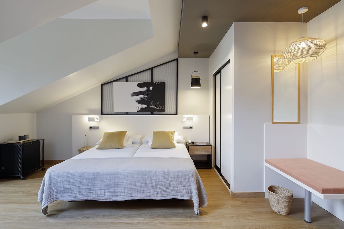 A modern bedroom with a large bed, a bench, and a wall-mounted light fixture.
