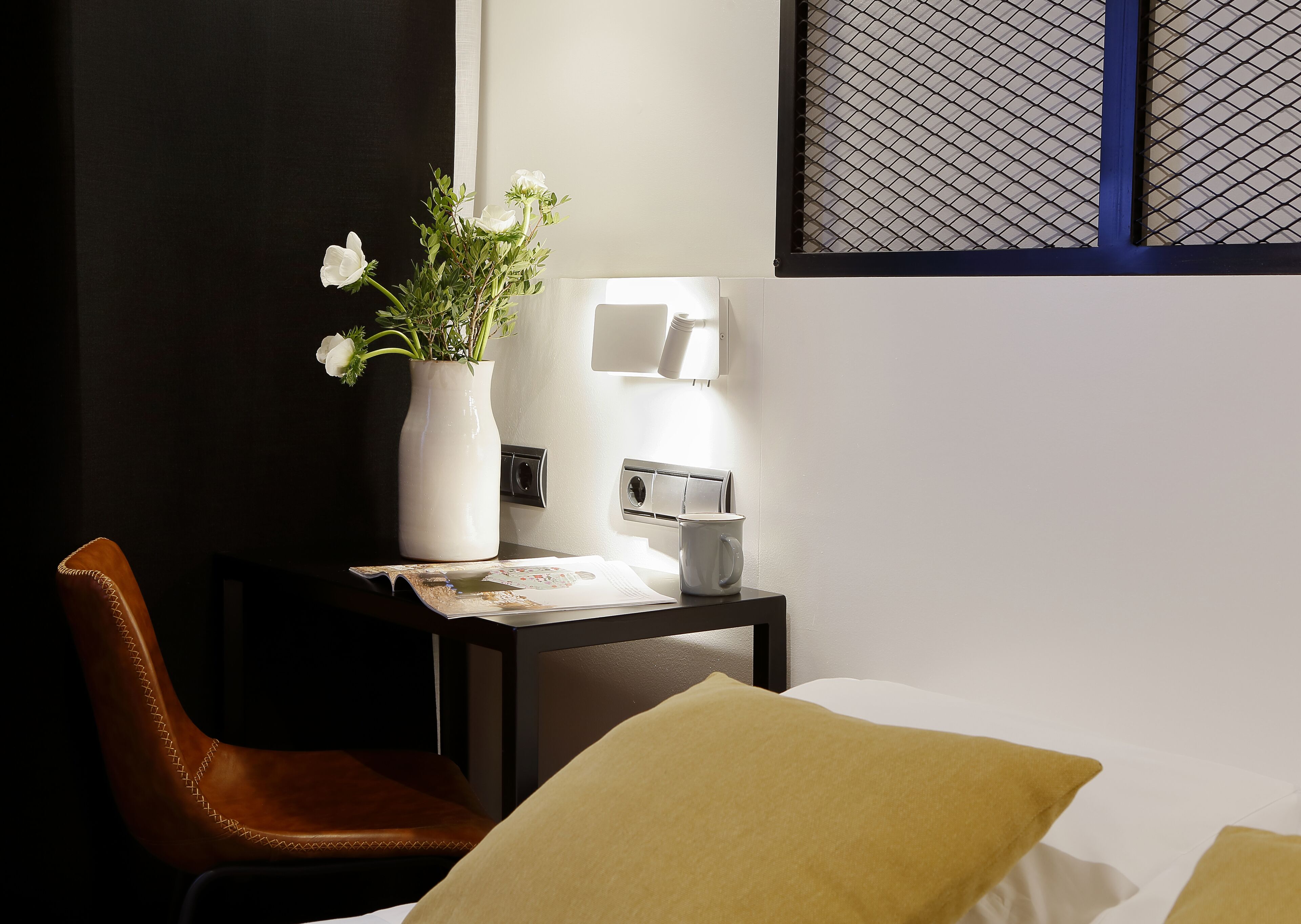 Habitación de hotel con escritorio, una silla, un jarrón con flores, una lámpara y una cama con almohadas.