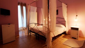 Un dormitorio con cama con dosel, mesita de noche, televisor y refrigerador.