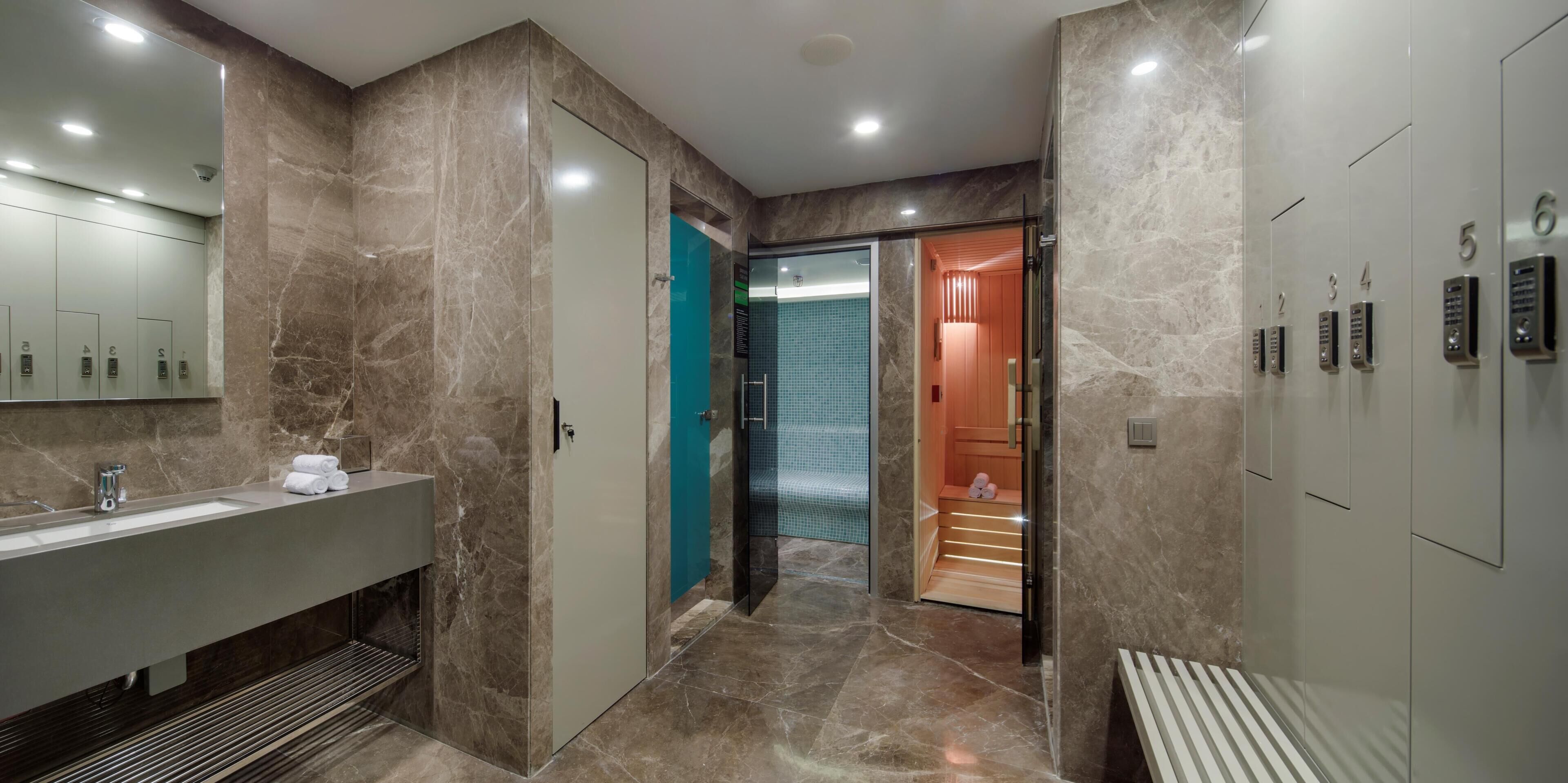 Un baño moderno con tocador de mármol, cabina de ducha de vidrio y una sala de sauna.