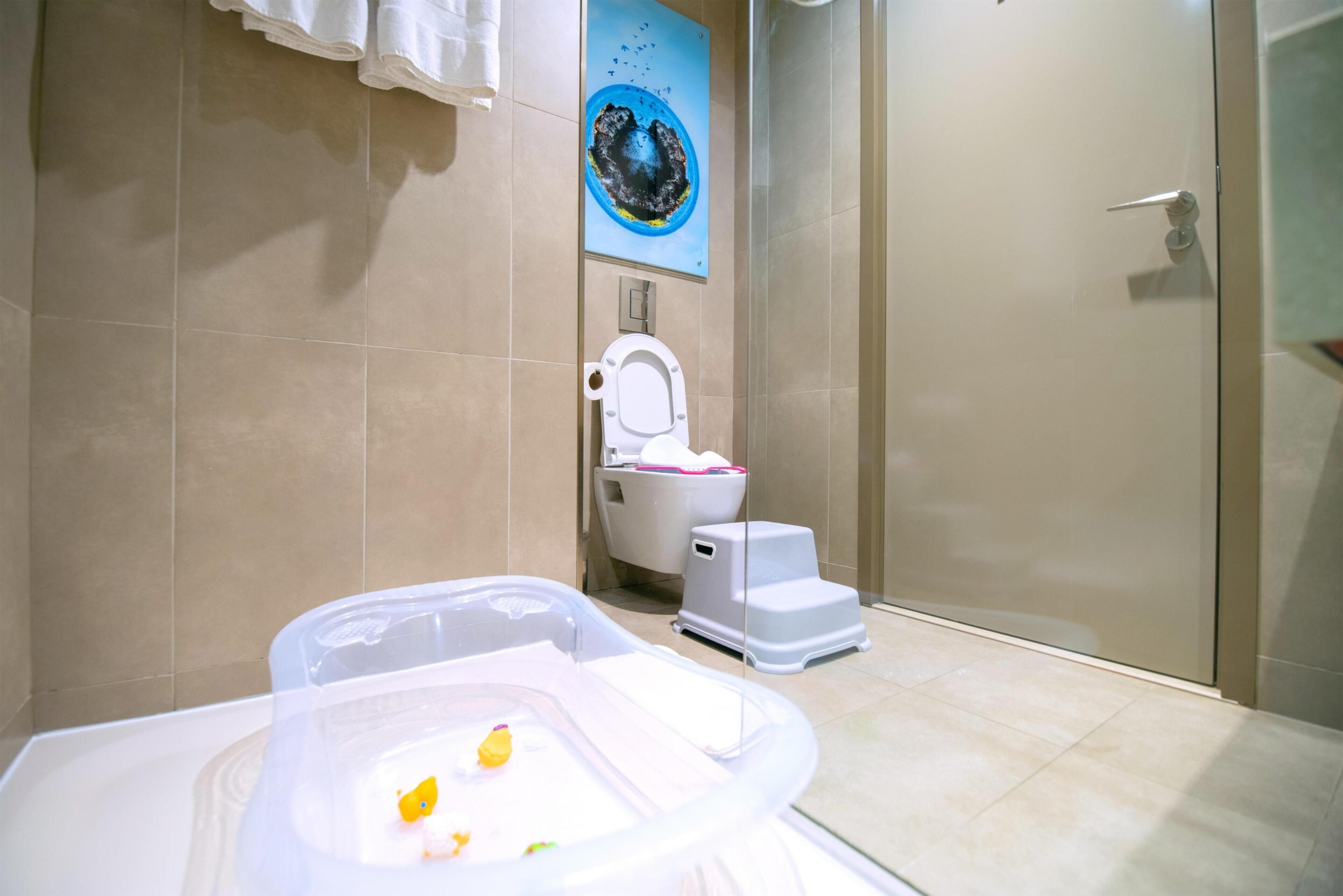 Een badkamer met een toilet, een douche en een bad met een plastic bak.