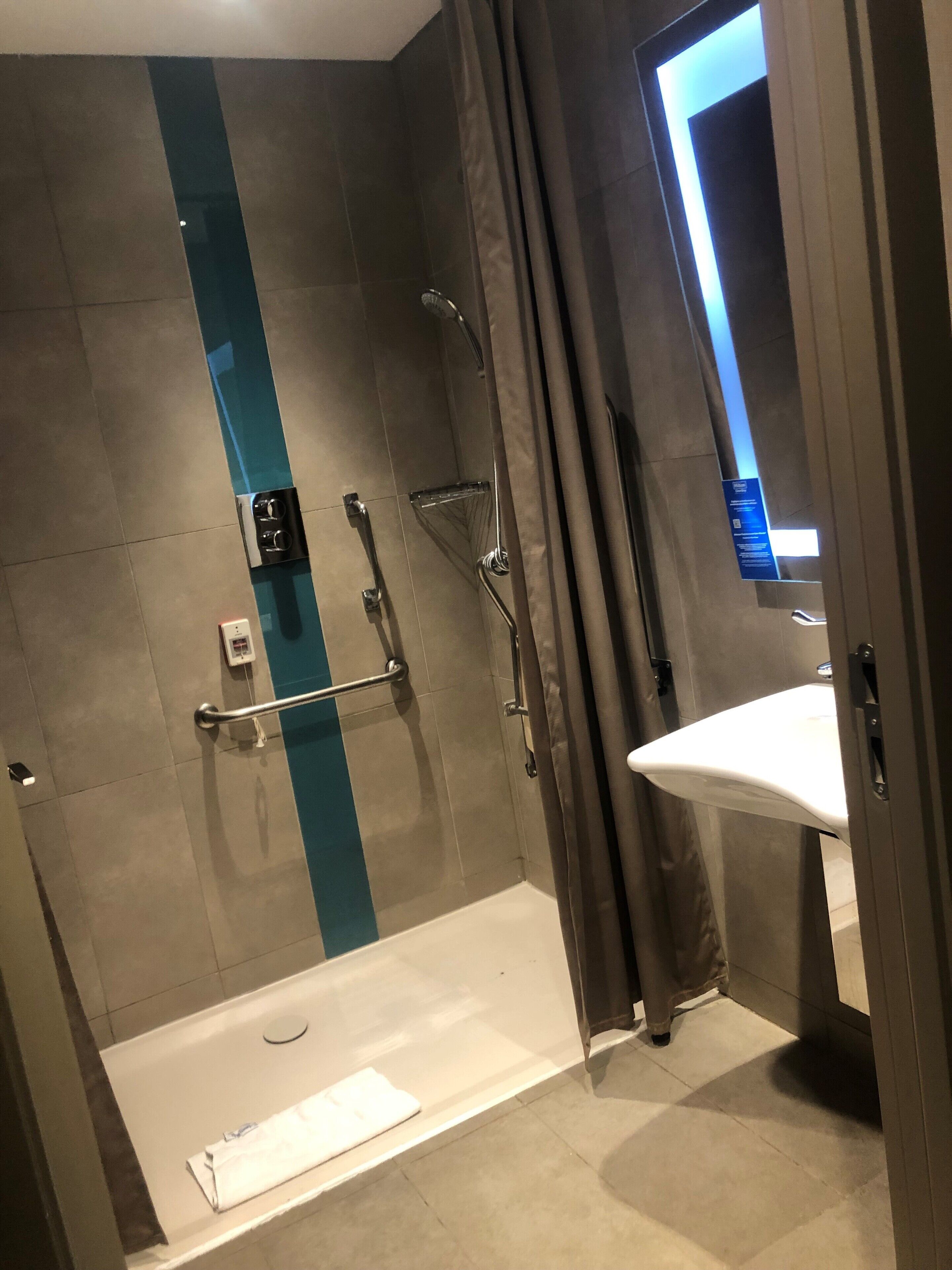 Une salle de bain moderne avec une douche à l’italienne, des barres d’appui et un lavabo blanc.