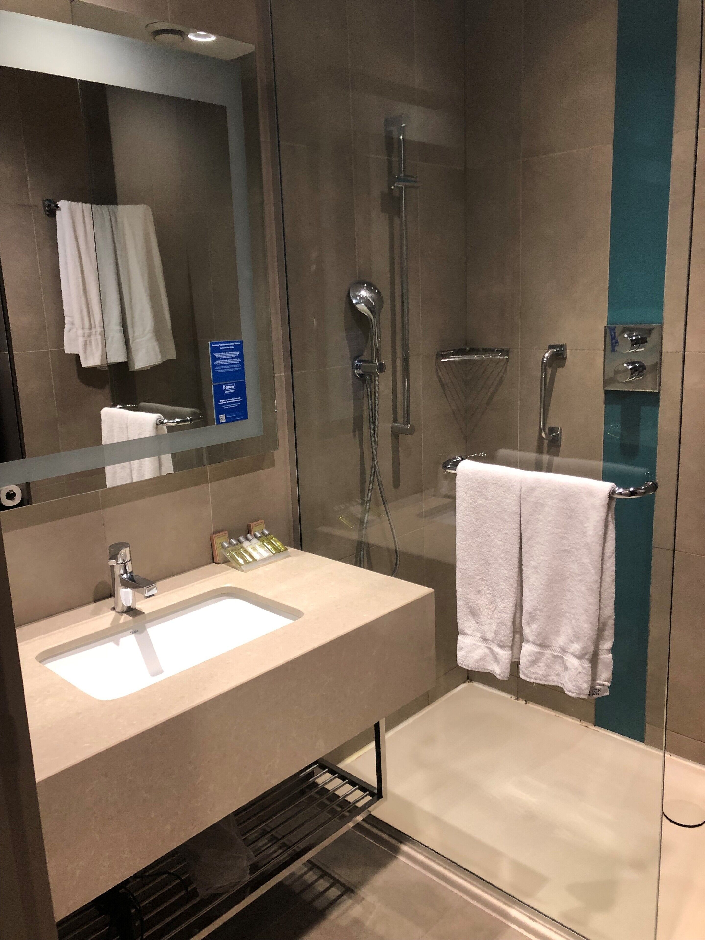 A modern bathroom with a glass-enclosed shower, a sink with a mirror above, and a towel rack.