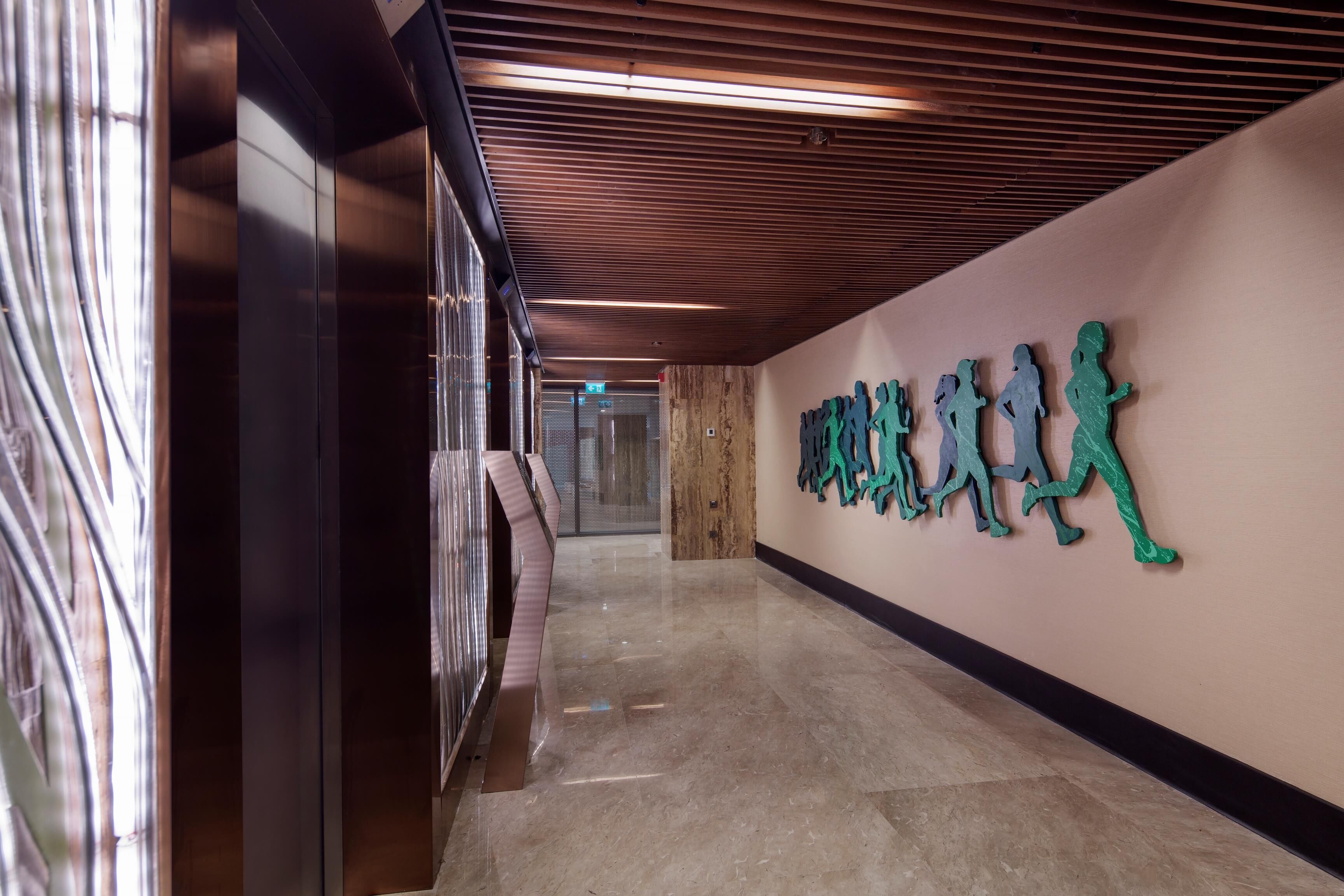 A corridor with a wooden ceiling, a wall with green silhouettes, and a shiny floor.