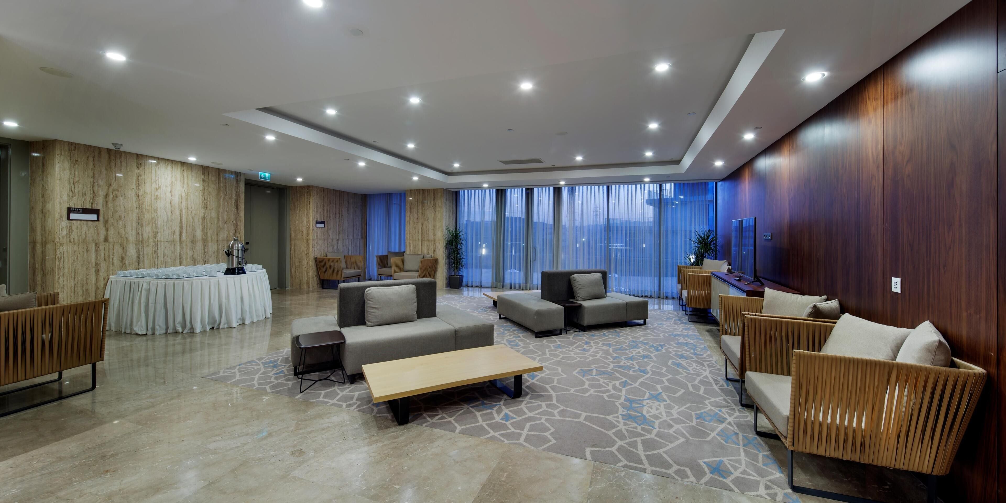 A modern lobby with a reception desk, sofas, a coffee table, and a patterned carpet.