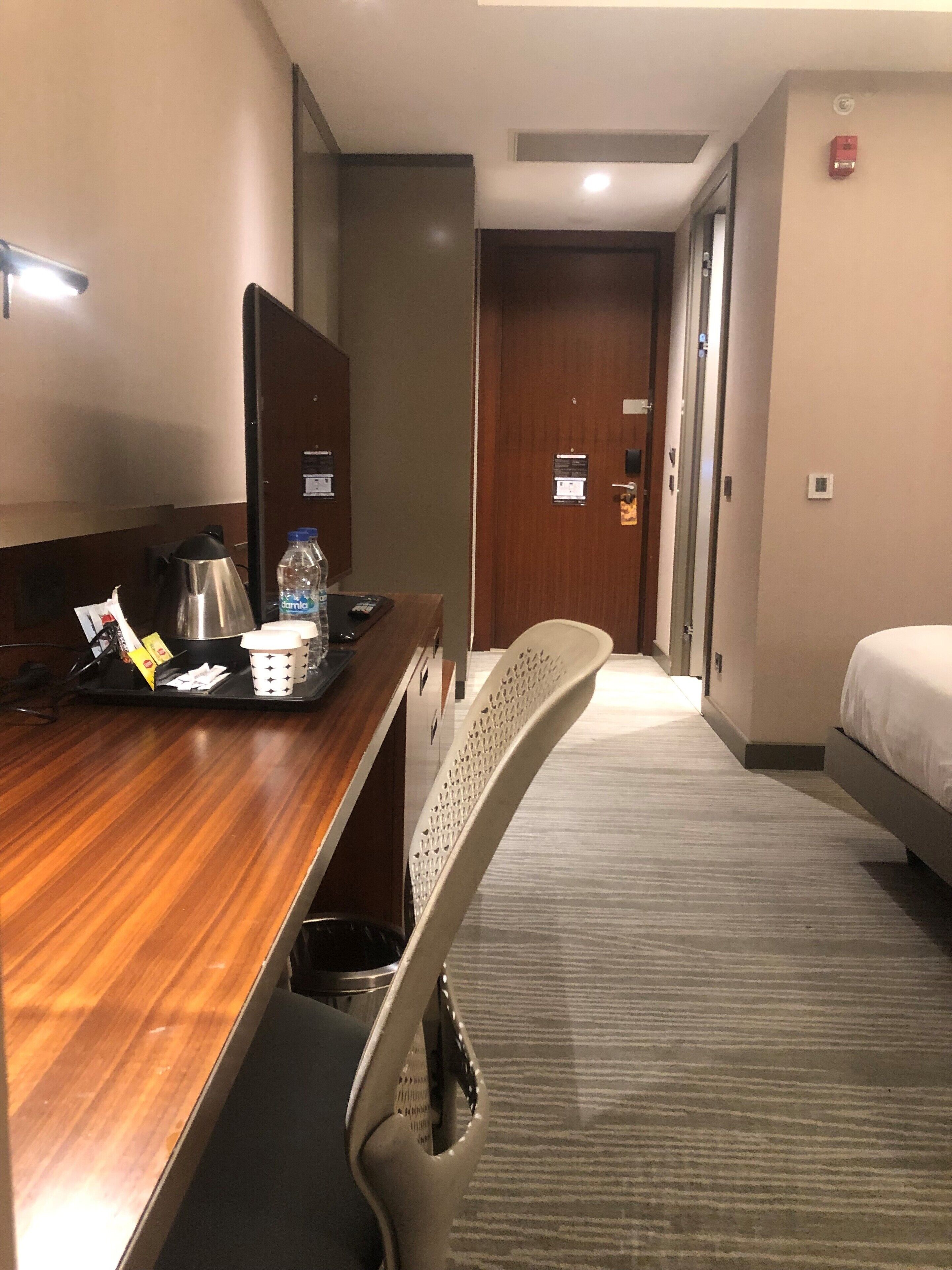 A hotel room with a wooden desk, a chair, a bed, and a carpeted floor.