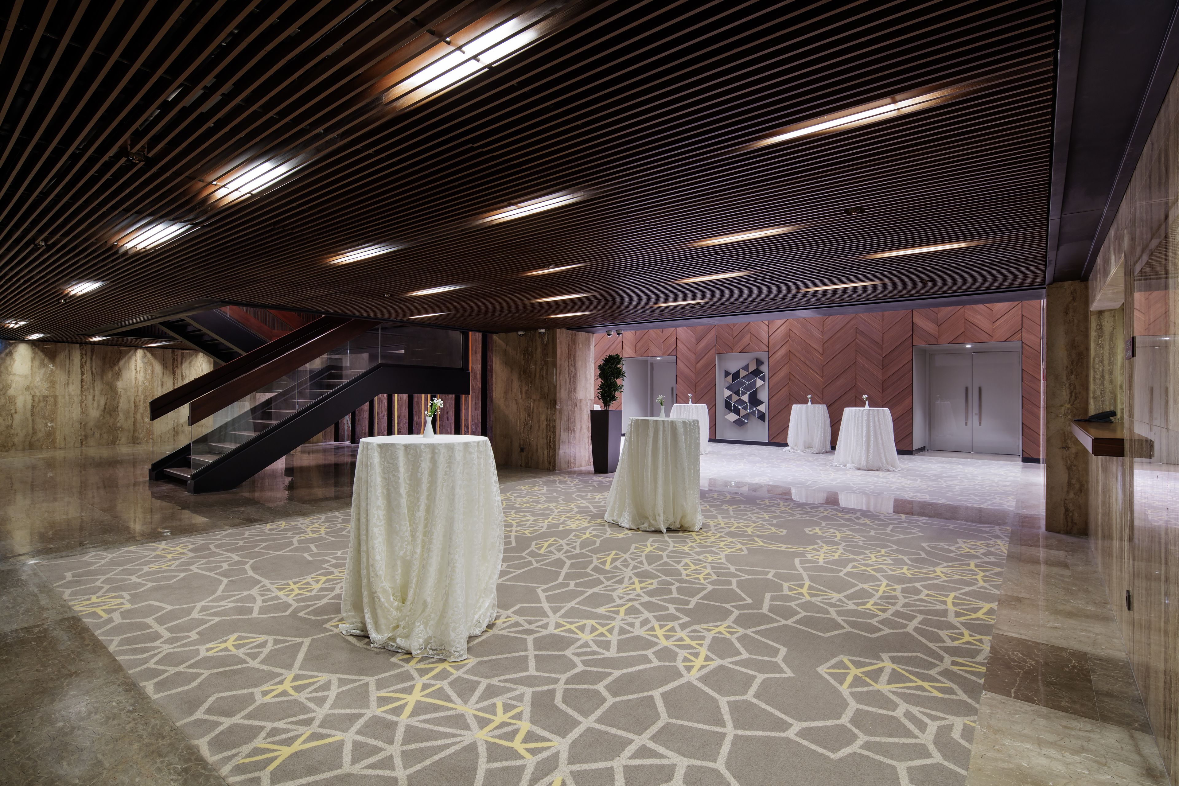 Een ruime lobby met een modern design, met een patroon vloer, een trap en meerdere ronde tafels.