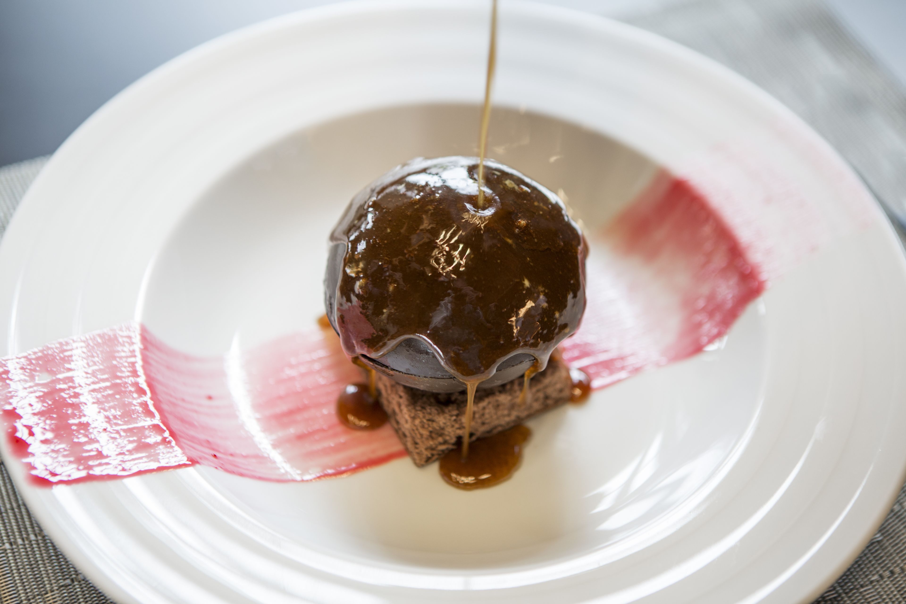 A dessert on a white plate with a caramel sauce being poured over it.