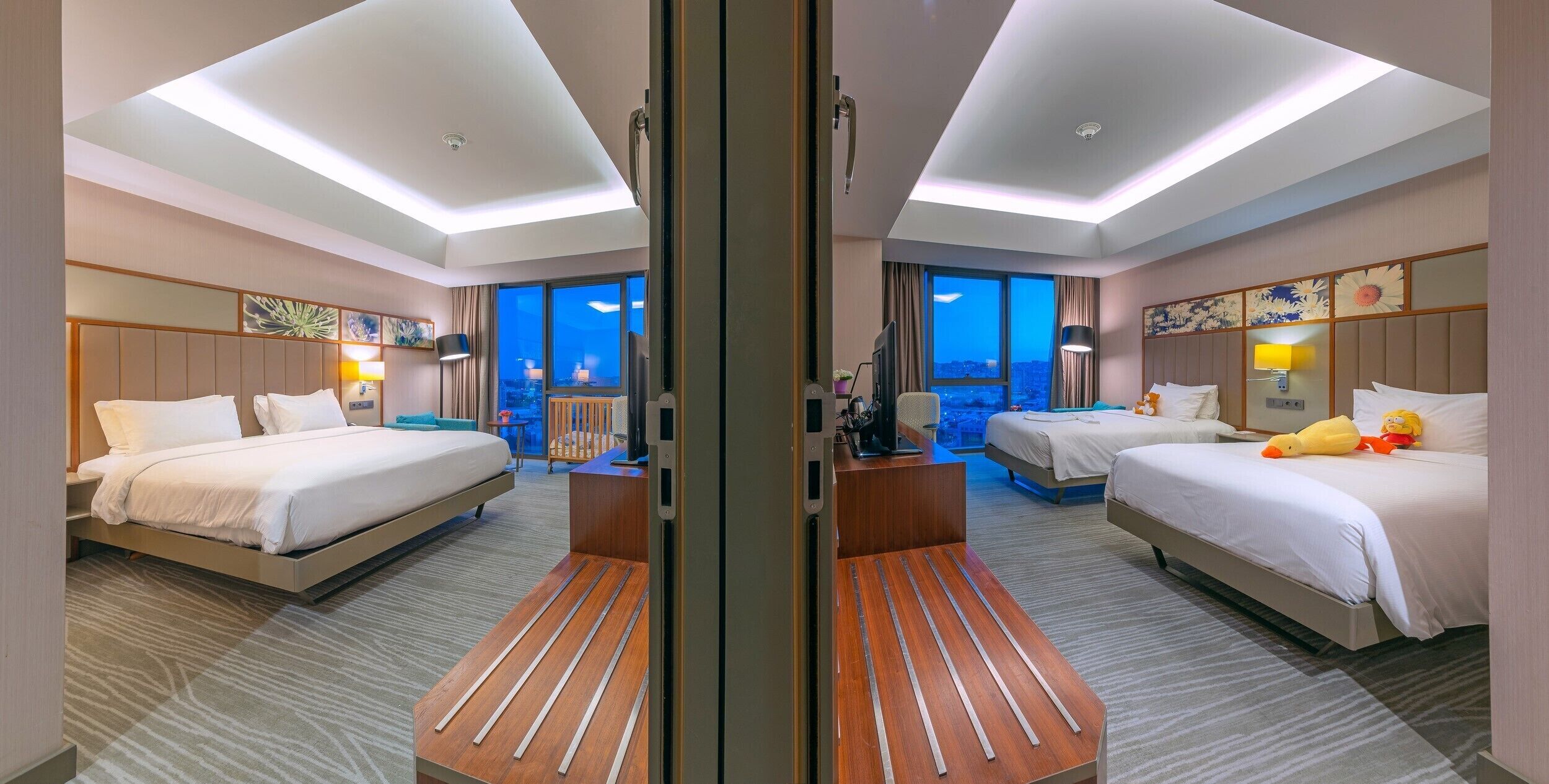 A hotel room with two beds, a desk, a chair, and a large window with a city view.