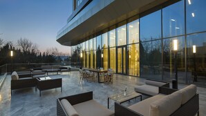 An outdoor patio area with seating and tables, large windows, and a modern building facade. - Hilton Garden Inn Istanbul Airport (Istanbul)