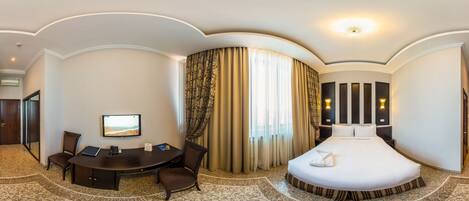 A hotel room with a curved ceiling, a desk with a chair, a bed with a white comforter, and a large window with curtains.