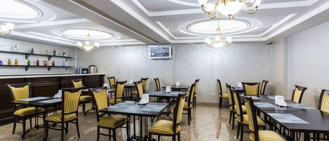 A conference room with a bar area, equipped with tables and chairs, and a television screen on the wall.