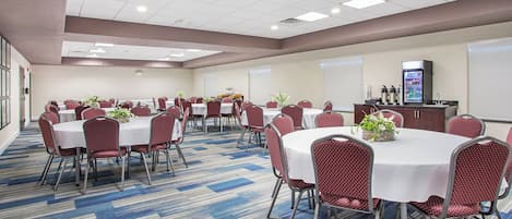 Un salón de conferencias con mesas redondas, sillas rojas y piso alfombrado.