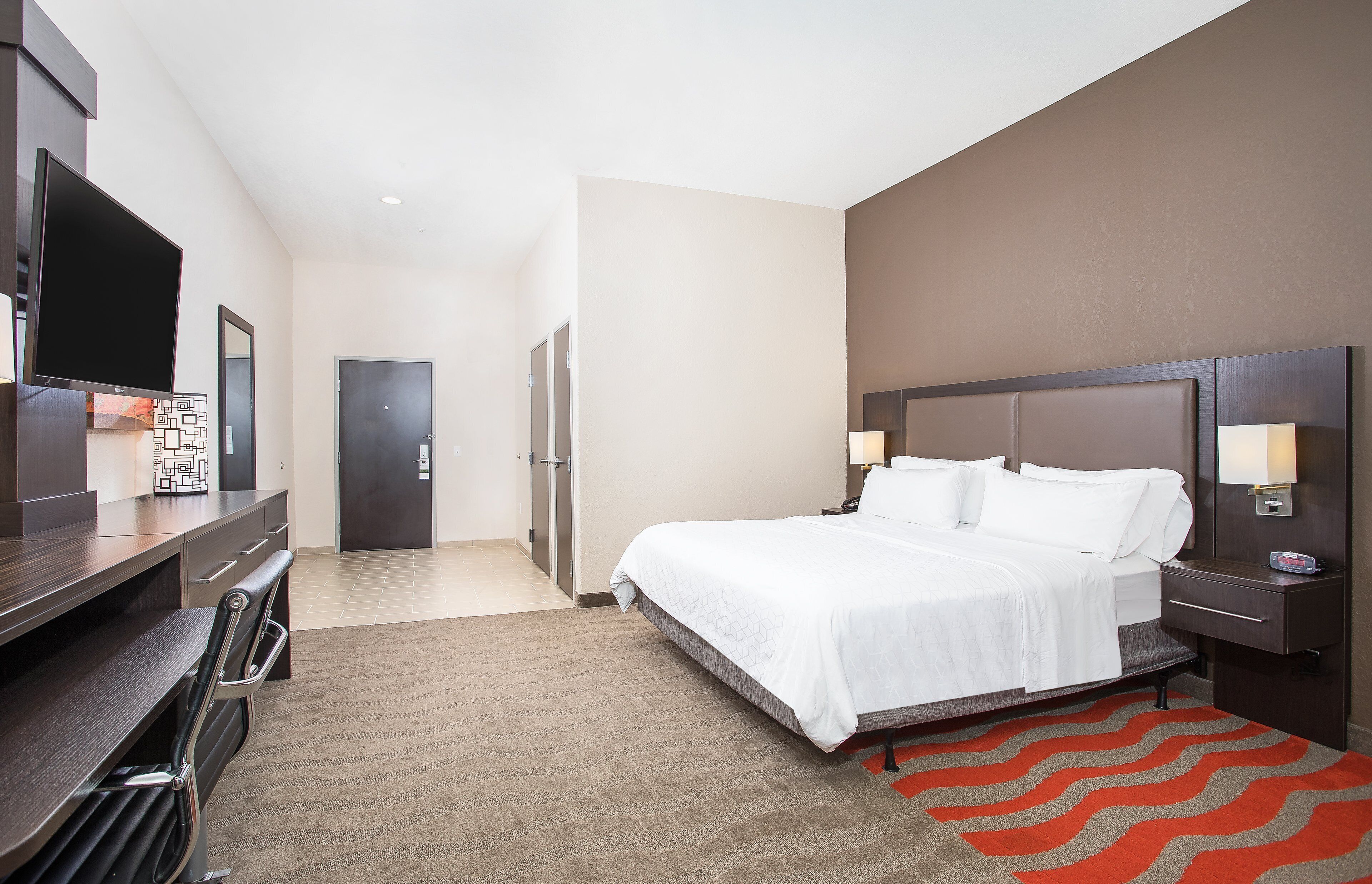 Una habitación de hotel con cama, mesitas de noche, escritorio, televisor y puerta.