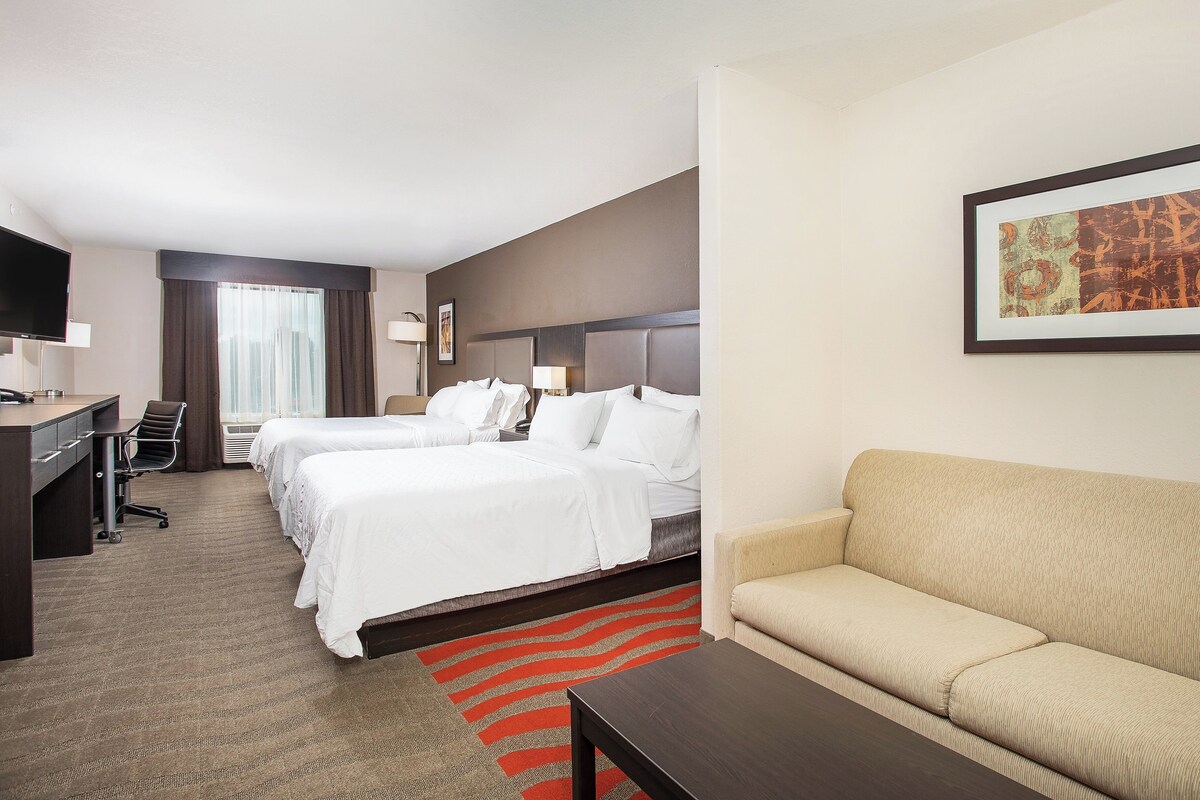 A hotel room with two beds, a desk, a chair, a sofa, and a TV.