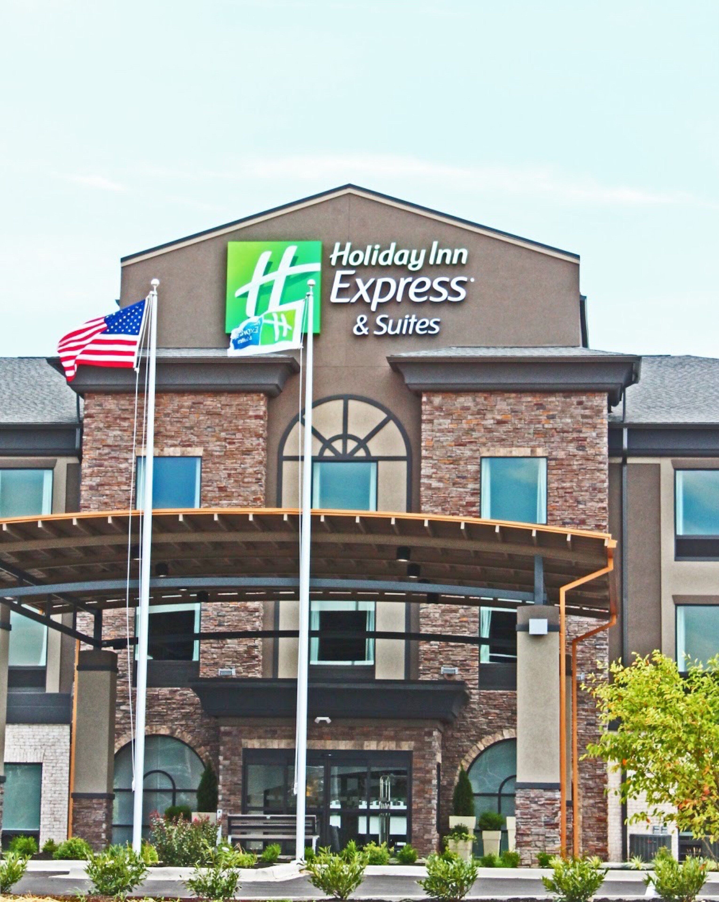 Un edificio de Holiday Inn Express & Suites con fachada de ladrillo, ventanas grandes y una bandera estadounidense.