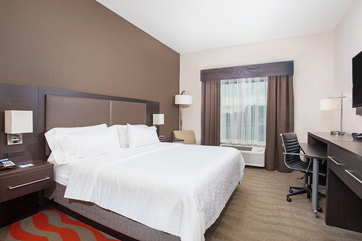 A hotel room with a large bed, a desk, a chair, and a TV.