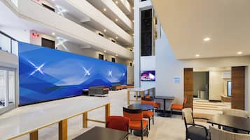 A modern interior with a high ceiling, multiple seating areas, and a large digital display.