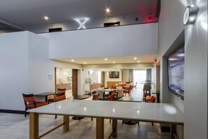 Une salle de conférence moderne, dotée d’une grande table et de nombreuses chaises, d’un téléviseur fixé au mur et d’un coin cuisine à l’arrière-plan.