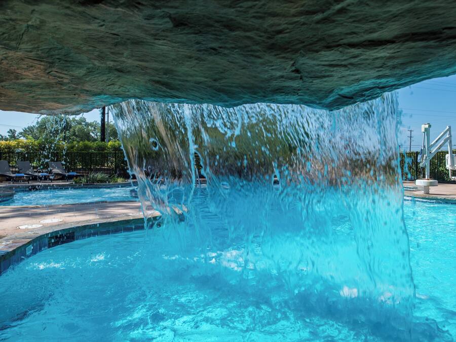 A pool with clear blue water, a waterfall feature, and lounge chairs in the background.