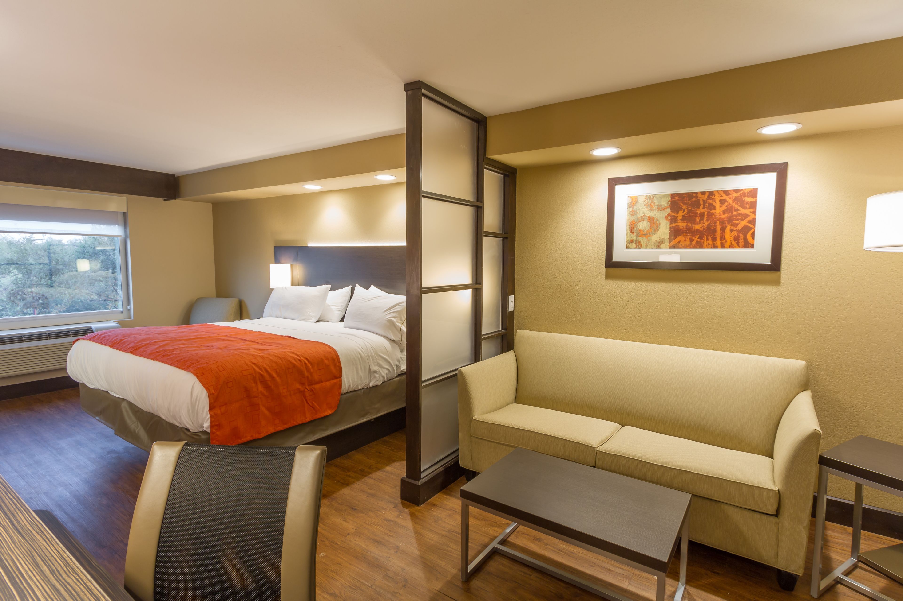 A hotel room with a bed, a sofa, a small table, and a window.