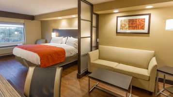 A hotel room with a bed, a sofa, a small table, and a window.