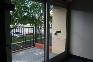 Vista a través de una puerta con reja metálica, un estacionamiento y un edificio al fondo.