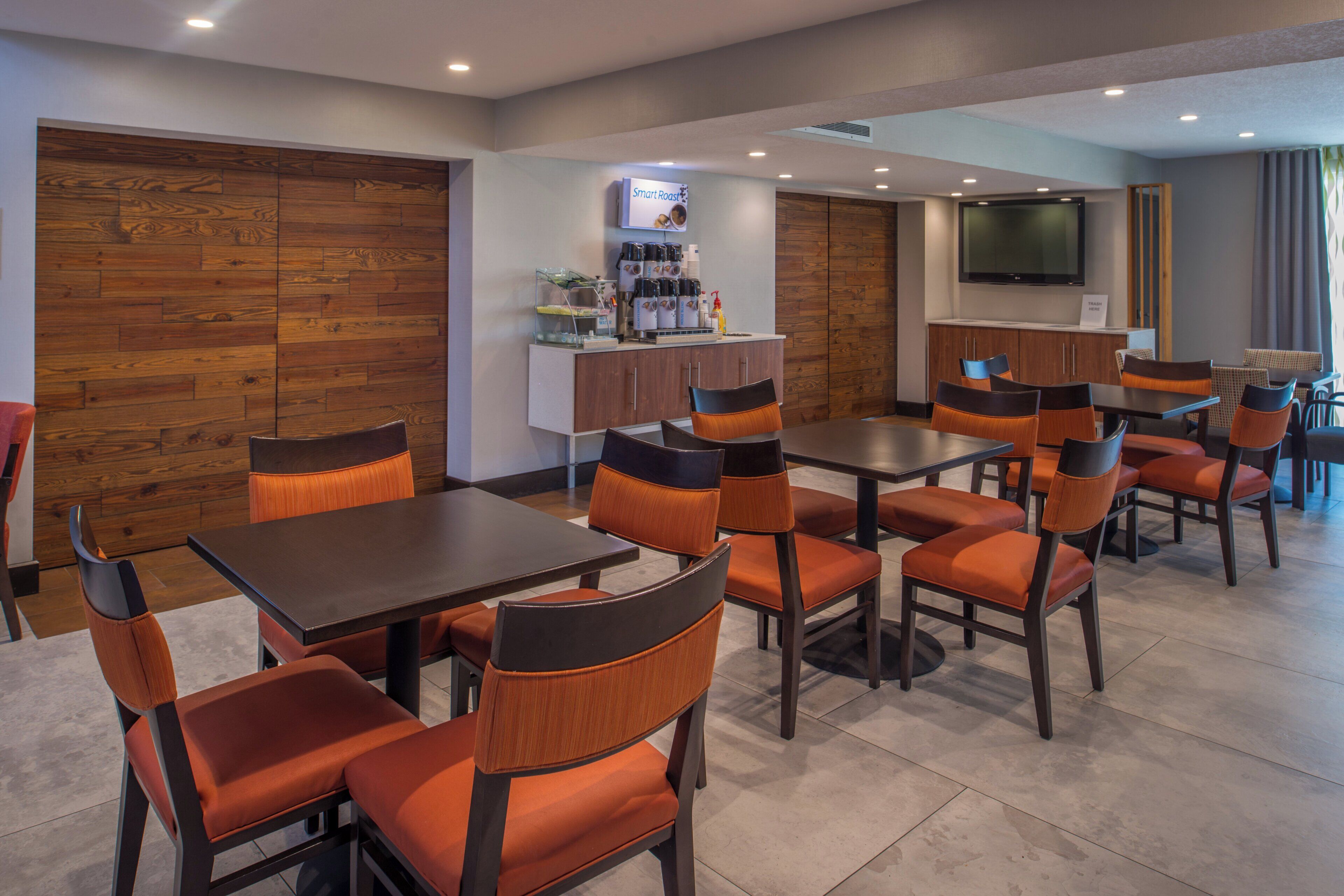 A modern dining area with wooden panel walls, a coffee station, and a flat-screen TV mounted on the wall.