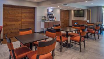 A modern dining area with wooden panel walls, a coffee station, and a flat-screen TV mounted on the wall.