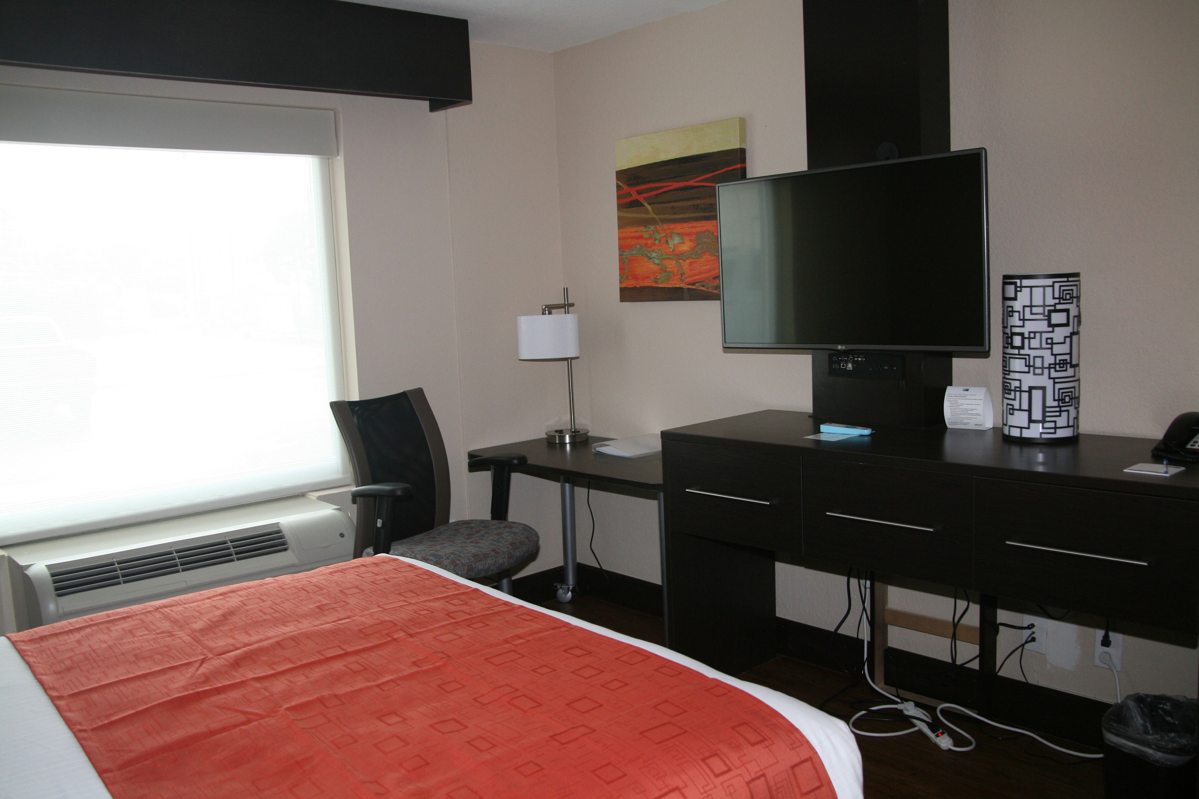 Una habitación de hotel con cama, escritorio, silla, televisor y ventana.