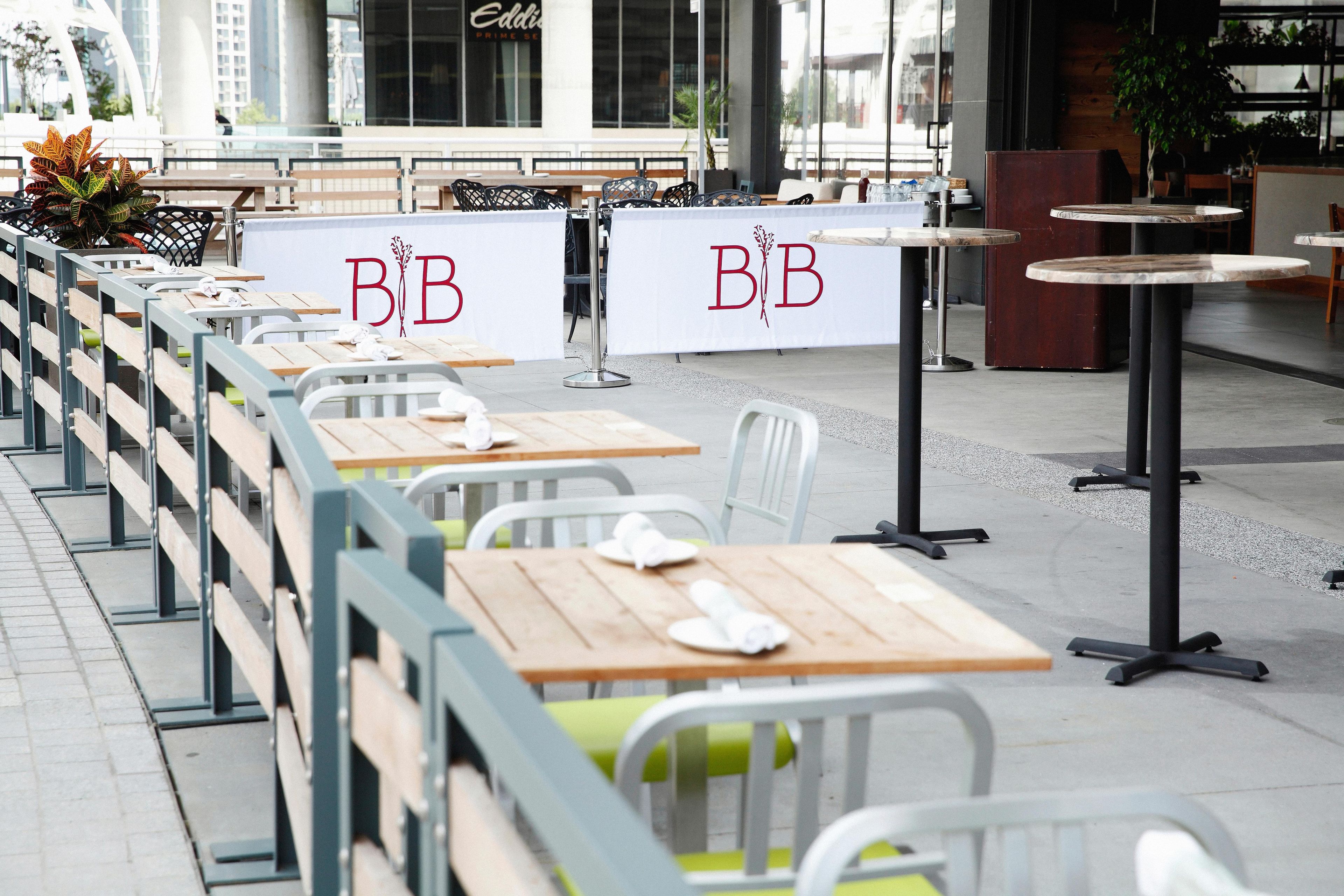 Outdoor seating with tables and chairs, a sign with 'B&B' lettering, and a building in the background.
