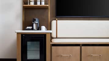 Una kitchenette con cafetera, un refrigerador pequeño y una alacena con botellas.