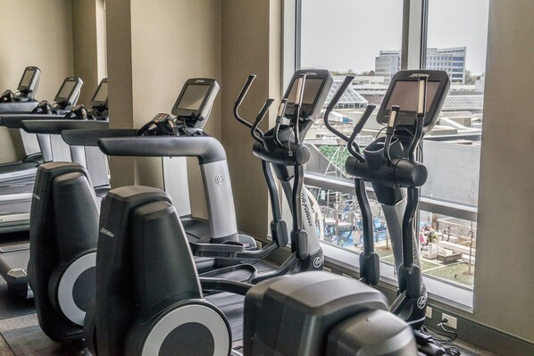 A gym with treadmills and elliptical machines, large windows with a view of buildings and a bridge.