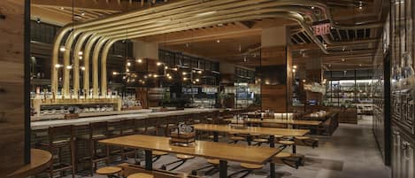 Un restaurant spacieux avec de hauts plafonds, des conduits apparents et différents types de sièges, notamment des tables et des banquettes.