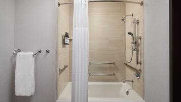 A modern bathroom with a bathtub, shower, and handrails.