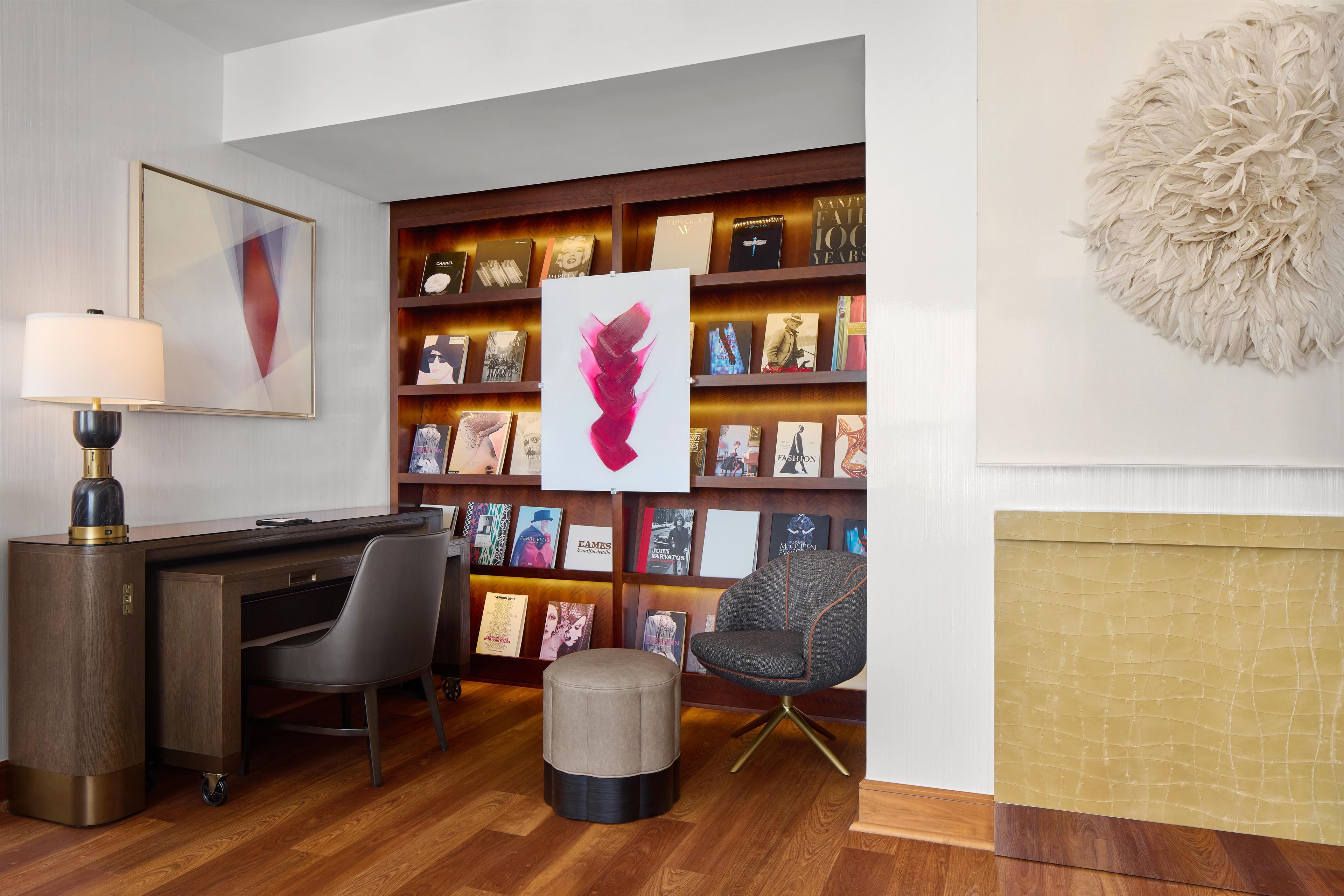 A modern library with bookshelves, a desk, a chair, and a decorative wall piece.