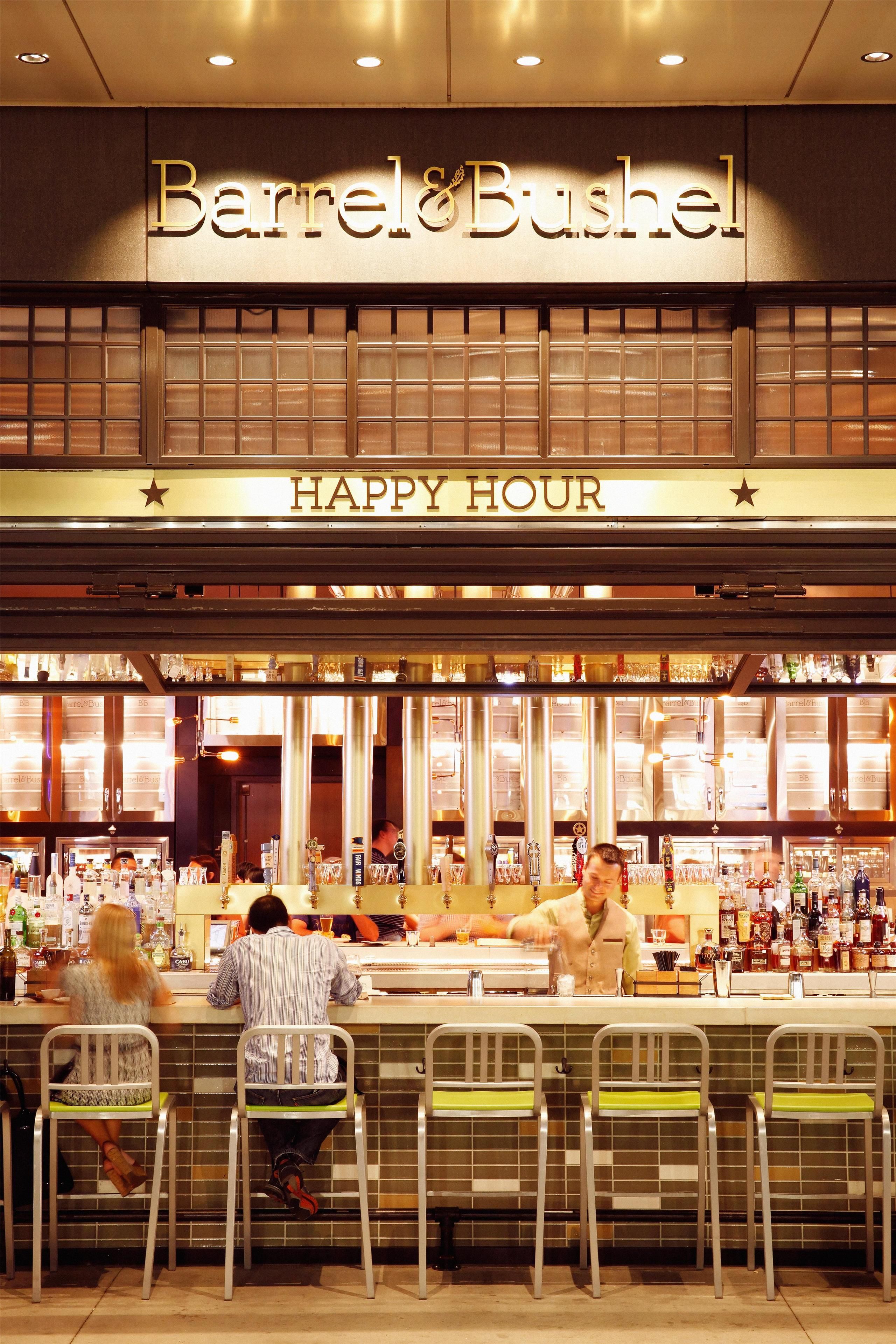 A bar named Barrel & Bushel with a 'Happy Hour' sign, bar stools, and a bartender.