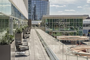 Terraza en la azotea con mobiliario exterior, un edificio de fachada de vidrio y cielo despejado.