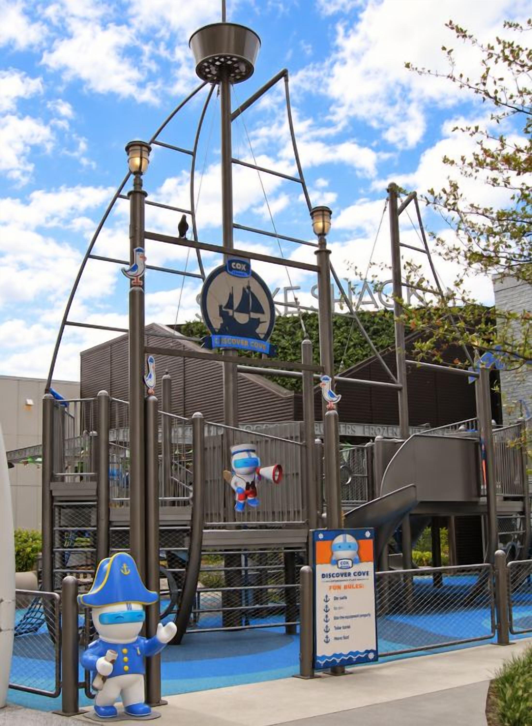 A playground with a ship-themed play structure, a blue mascot figure, and a sign indicating a discovery center.