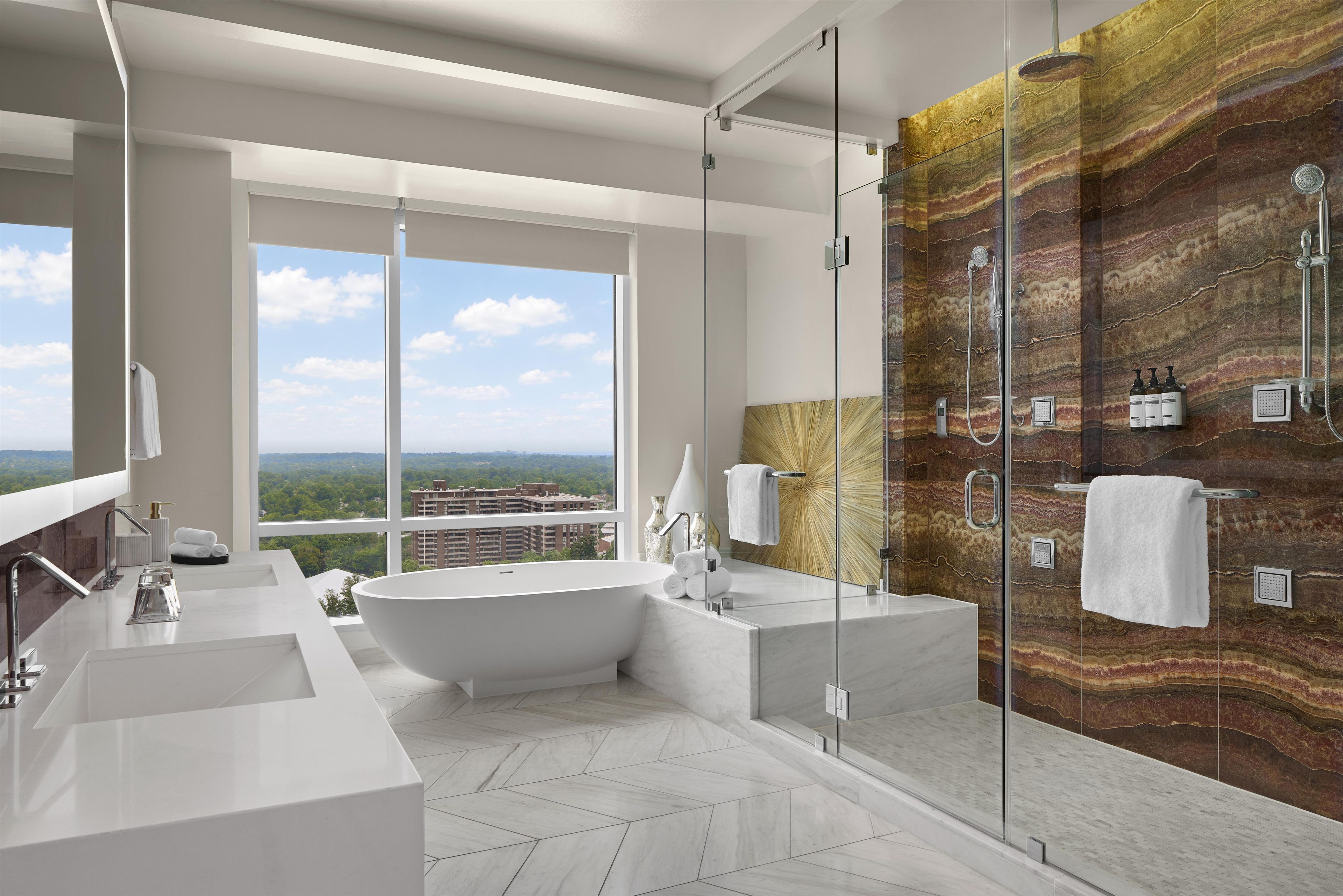 A modern bathroom with a freestanding bathtub, a glass-enclosed shower, and a large window offering a city view.