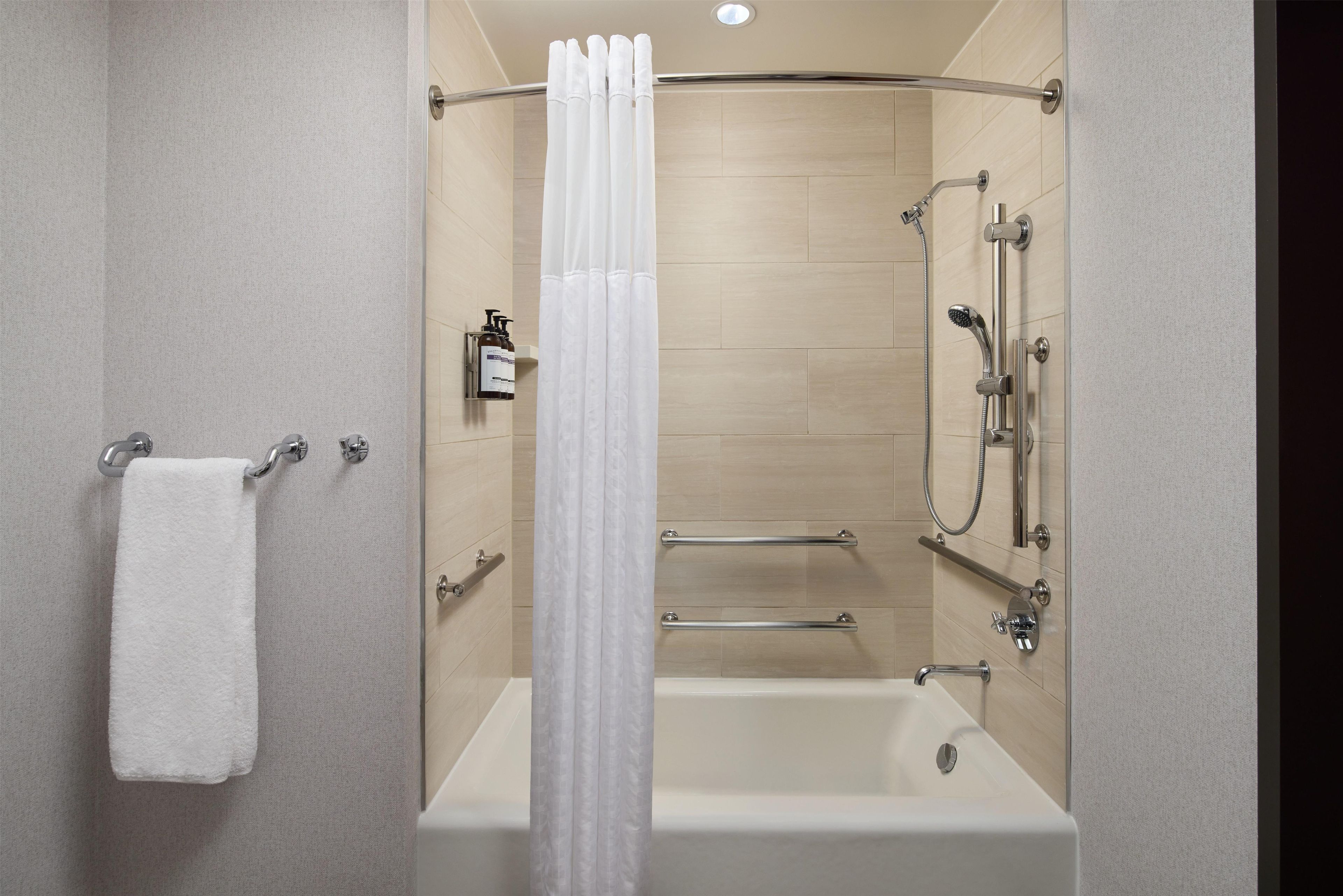 A modern bathroom with a bathtub, shower, and handrails.